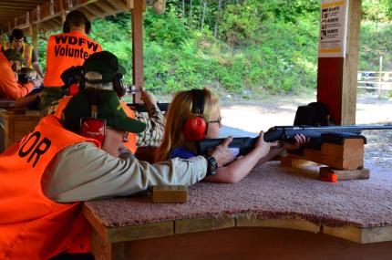Hunter education instructor showing young girl how to shoot a rifle safely.