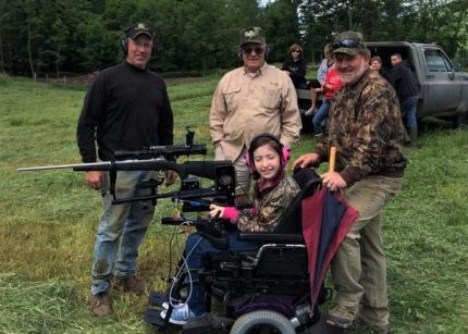 Young feamle hunter poses with adaptive equipment and mentors. 