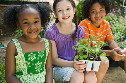 Three young children smile while holding plants