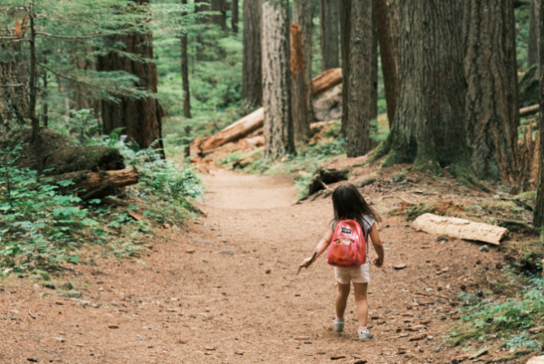 Child walks through woods wearing a backpack