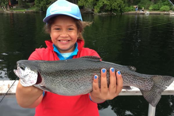 A young woman smiles while holding a trout she just caught.