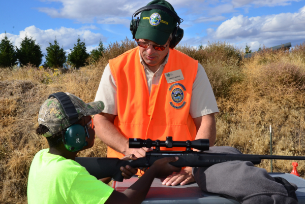 Hunter education instructor helps young person shoot.