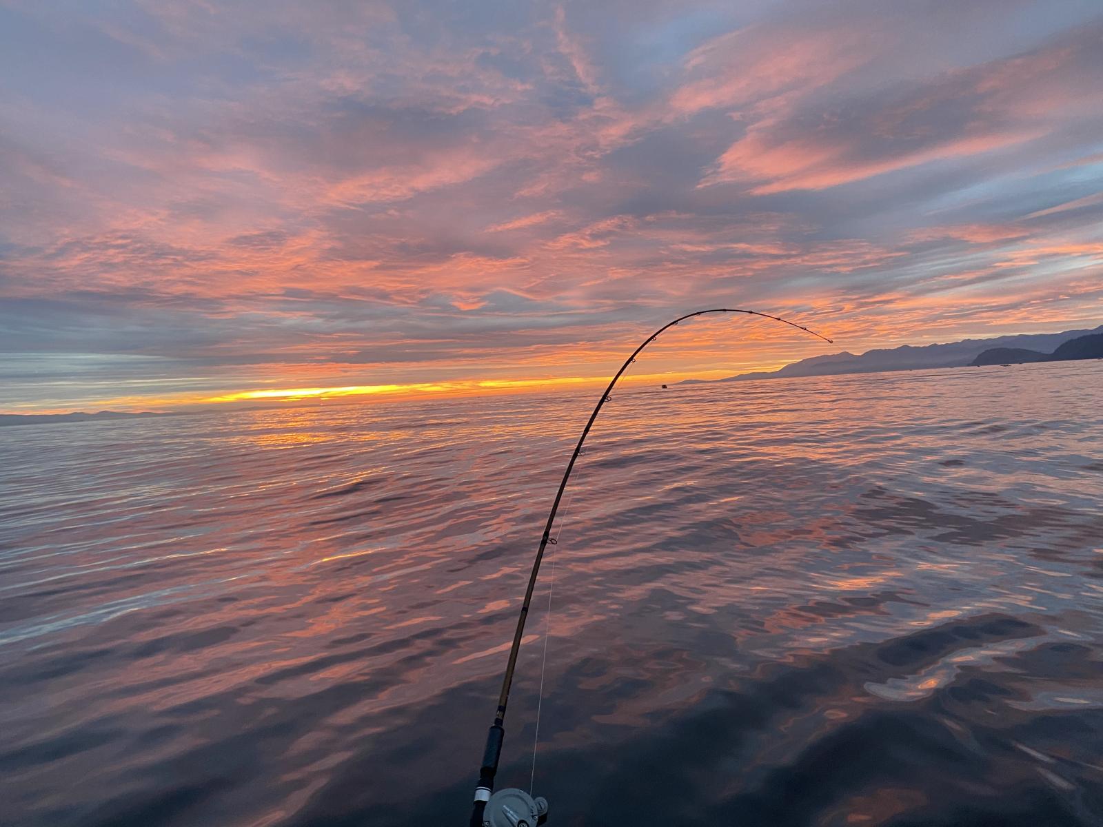 Sunrise over open water with fishing rod in center