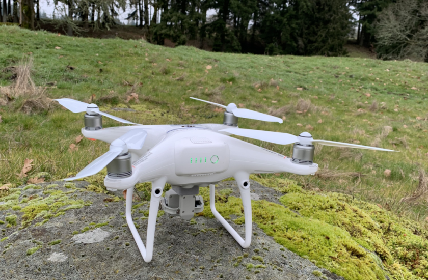 A white drone landed on a large rock in a forest clearing.