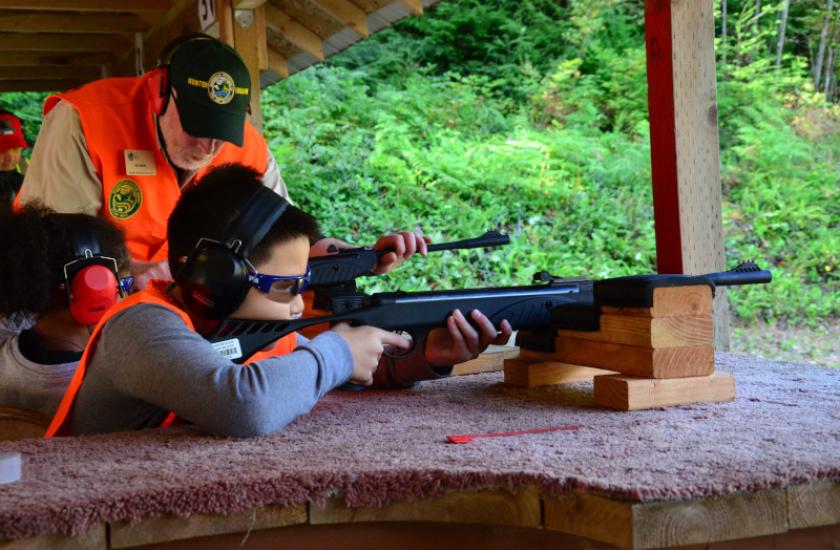 Two young hunter education students practicing at a shooting range while an instructor stands nearby giving direction