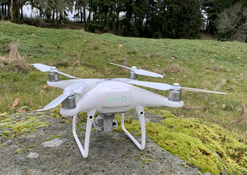 A white drone landed on a large rock in a forest clearing.