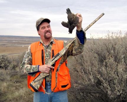 Photo of a hunter wearing a hunter orange vest holding a shotgun and a freshly harvested quail