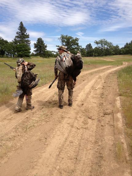 Father and son hunters walking down a dirt road, each carrying a turkey they harvested