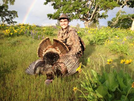 young man with harvested turkey and rainbow in distance.