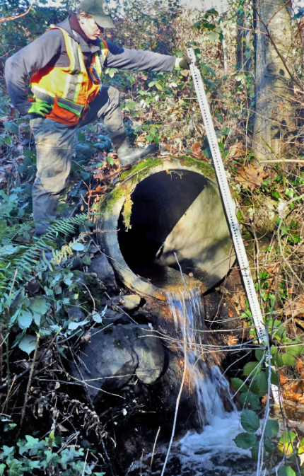 A person takes measurements of a culvert