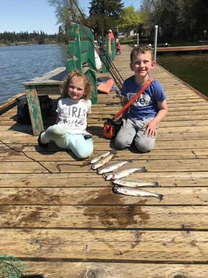 two young children sitting on a dock with several fish they have caught