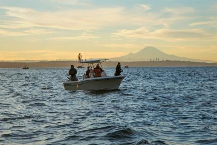 Four anglers fishing from a boat on Puget Sound with Mt. Rainier in the distance