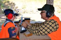 Hunter education instructor demonstrating safety procedures at shooting range with boy