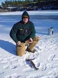 Man kneeling on the snow with a freshly caught trout