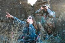 One adult and one youth look through binoculars toward wildlife 