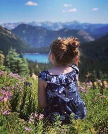 Girl sitting in wildflowers overlooking alpine lake mountain landscape