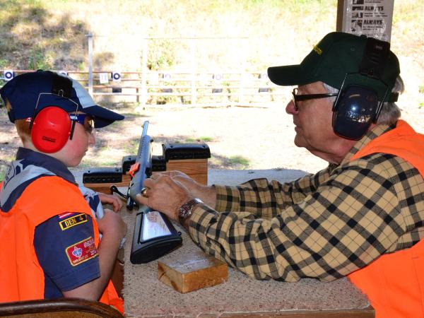 A volunteer teaching a hunter education course shows a young course participant details of a practice rifle on a table.