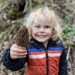 A three-year-old boy grins as he holds up his first-ever morel for the camera.