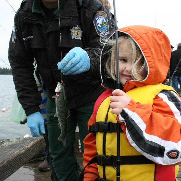 An officer stands with a little girl holding a fish